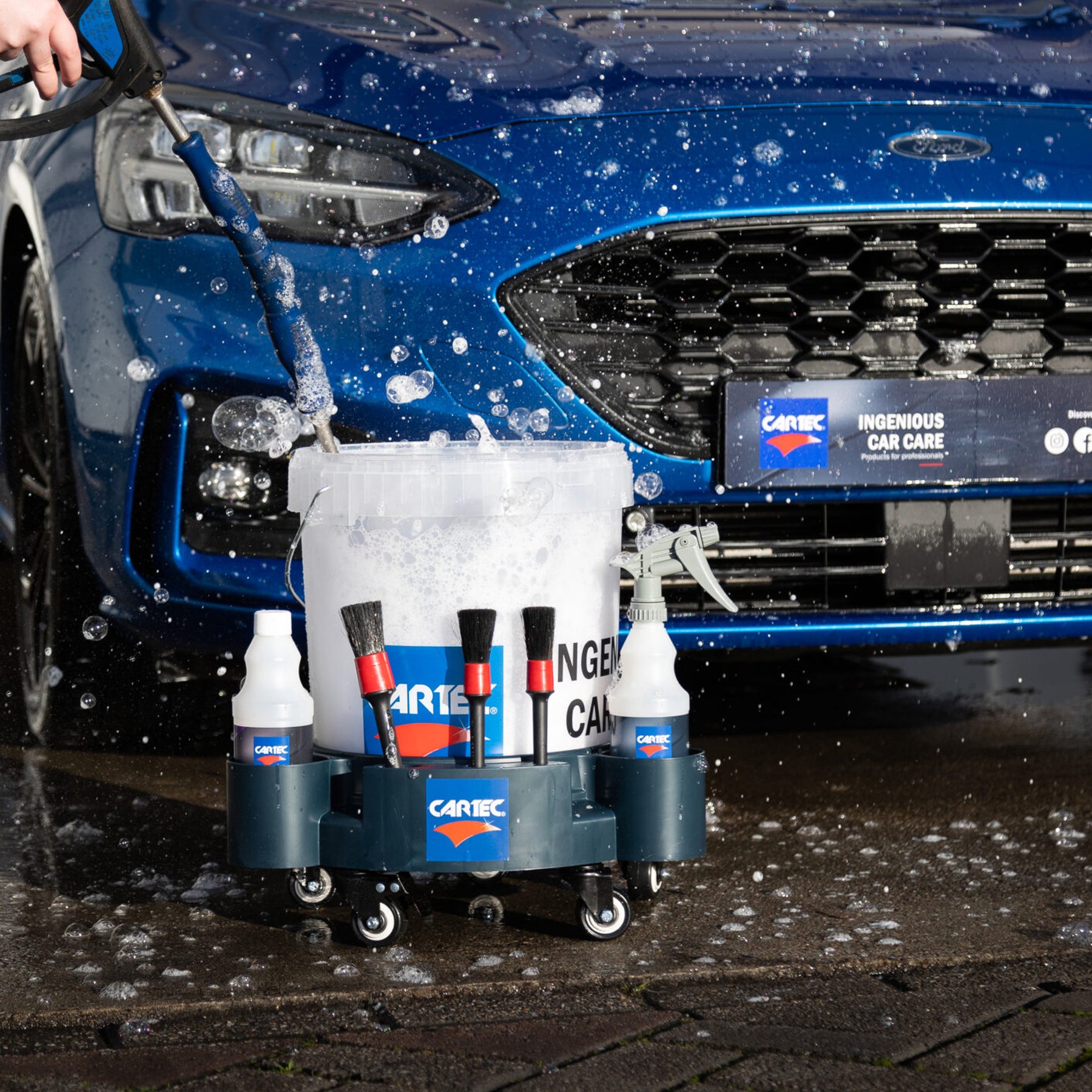 Secchio CARTEC Dolly Bucket con rotelle, pieno di accessori per il lavaggio, accanto a un'auto blu durante il lavaggio.