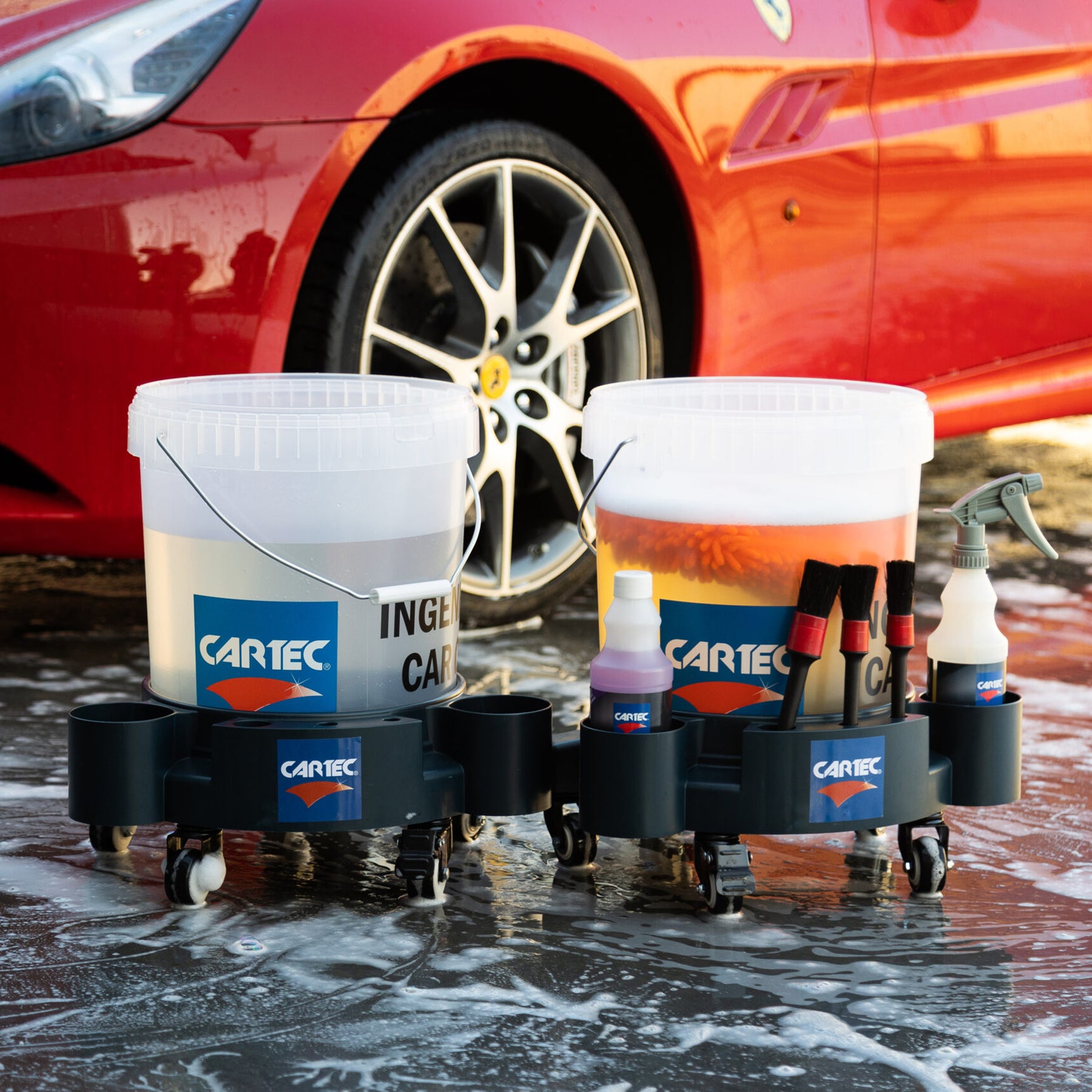 Kit professionale di lavaggio auto Cartec con secchi e accessori davanti a una Ferrari rossa.