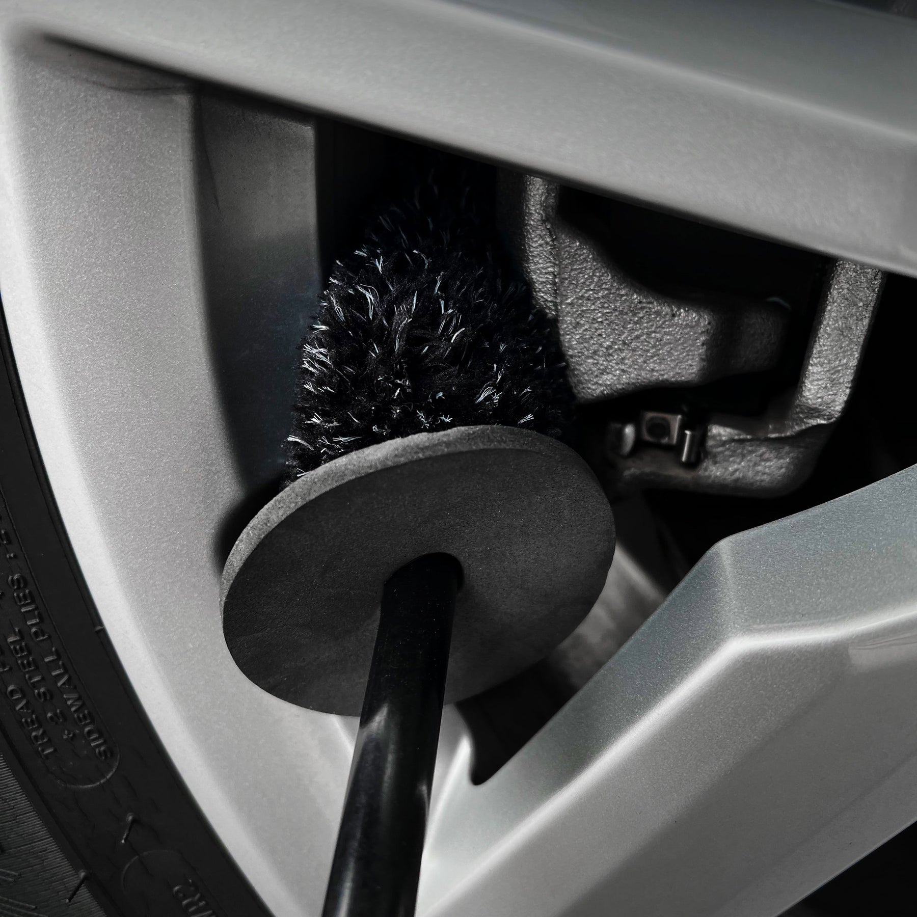 spazzola CARPRO Flat & Spot Brush con setole nere mentre pulisce una parte interna di un cerchione di un'auto. Le setole stanno rimuovendo lo sporco da un'area difficile da raggiungere, dimostrando la precisione della spazzola nel trattare i dettagli.