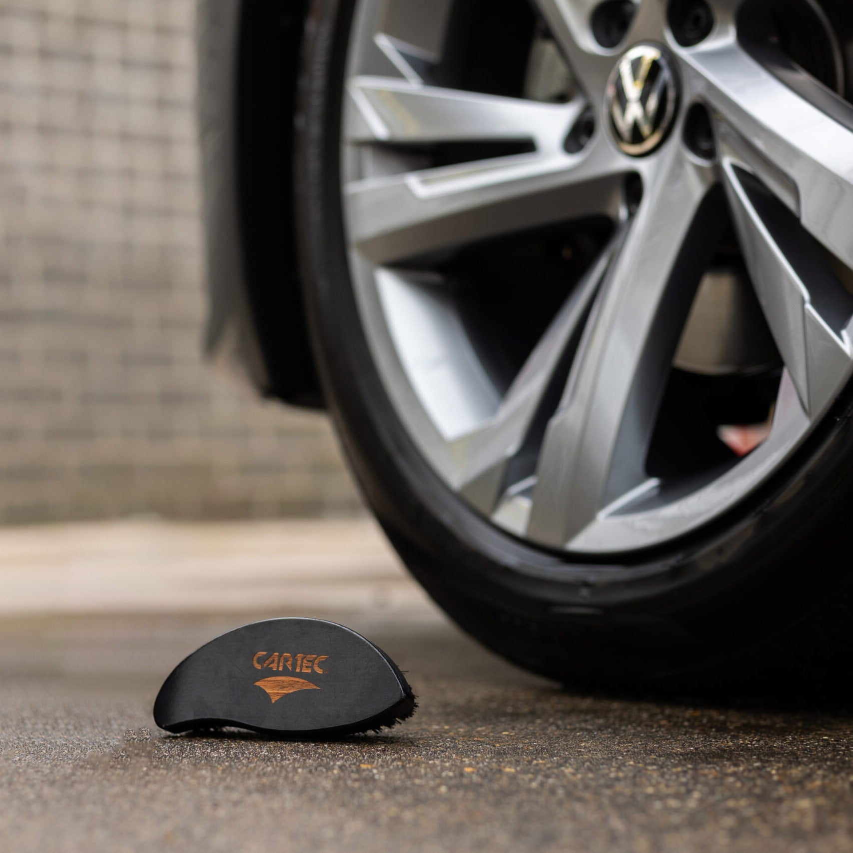 Mano con guanto nero che utilizza la spazzola CARTEC Dynamic Tyre Brush per pulire un pneumatico.