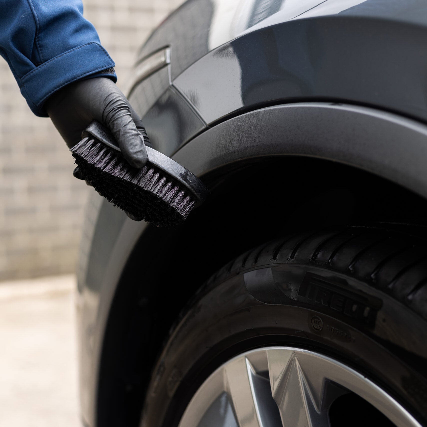 Mano con guanto nero che utilizza la spazzola CARTEC Dynamic Tyre Brush per pulire il pneumatico di un'auto.