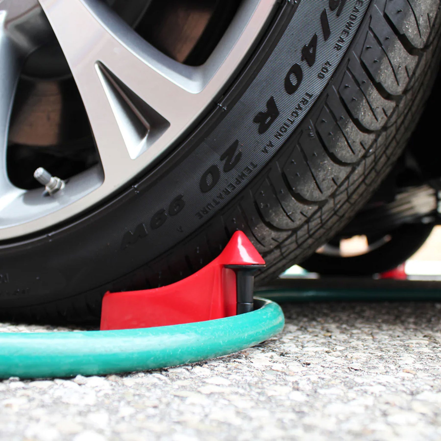 Hose Guide rosso Detail Guardz posizionato accanto a una ruota per evitare che il tubo si impigli durante il lavaggio dell'auto.