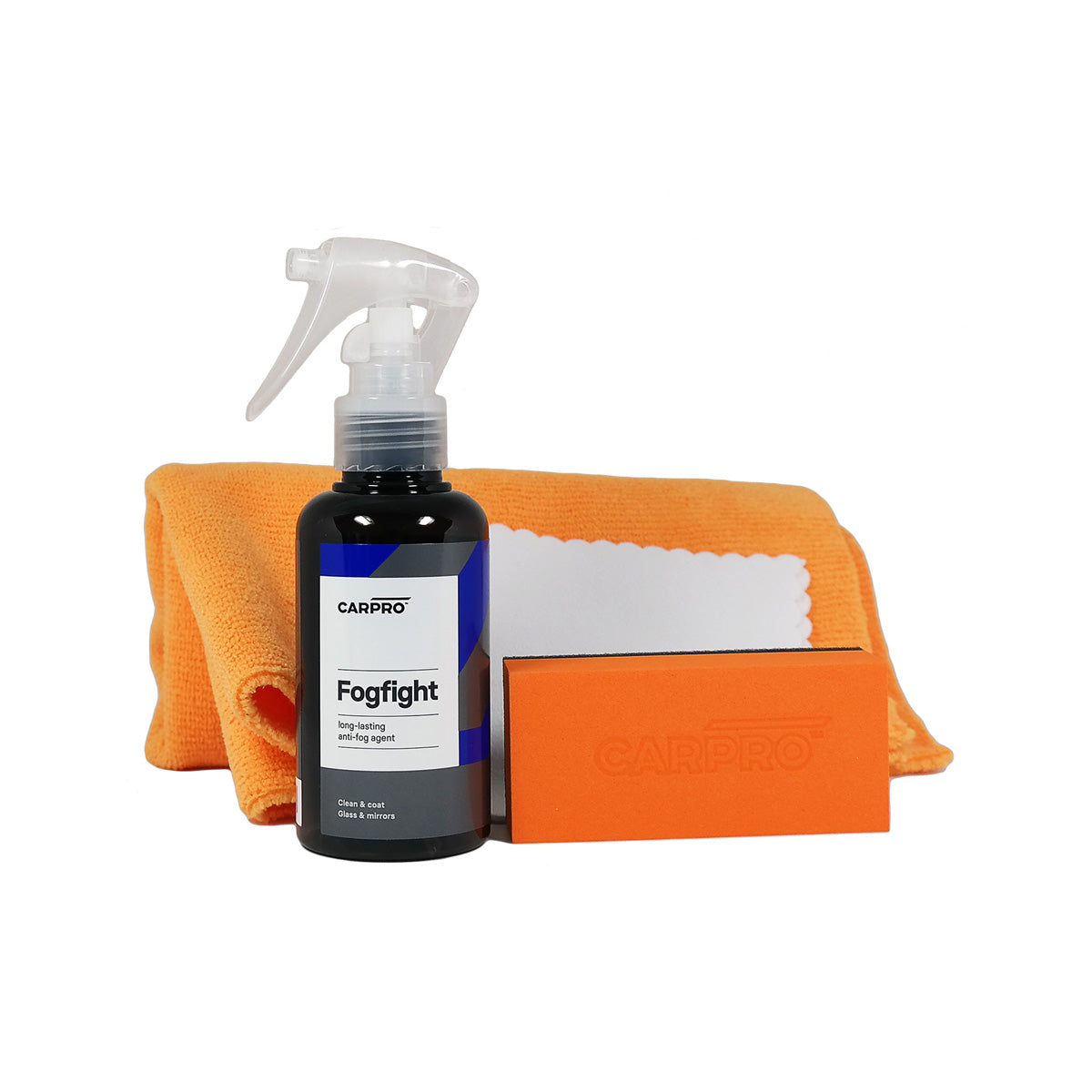 L'immagine mostra il kit CARPRO Fog Fight, che include un flacone spray di trattamento antiappannamento, un panno arancione, un blocchetto applicatore arancione e un panno bianco per la pulizia dei vetri.