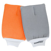 L'immagine mostra due guanti CARPRO GlassMitt per la pulizia dei vetri. Il guanto a sinistra è arancione con una texture a nido d'ape, mentre quello a destra è grigio con una superficie liscia. Entrambi i guanti hanno un bordo bianco elastico con il logo CARPRO stampato.