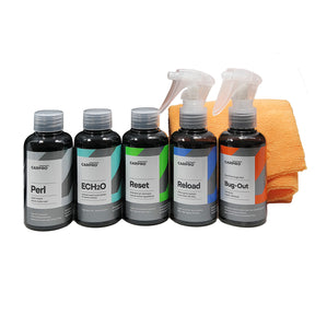 Set di cinque flaconi di prodotti per la manutenzione auto CARPRO con due panni in microfibra arancioni su sfondo bianco.  